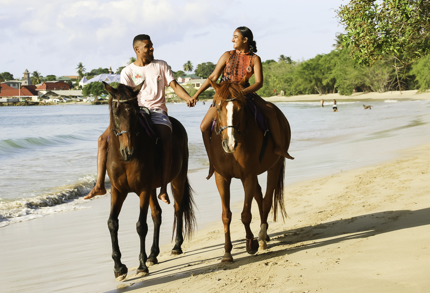 Par, der rider på heste på en sandstrand i tobago og holder hinanden i hånden