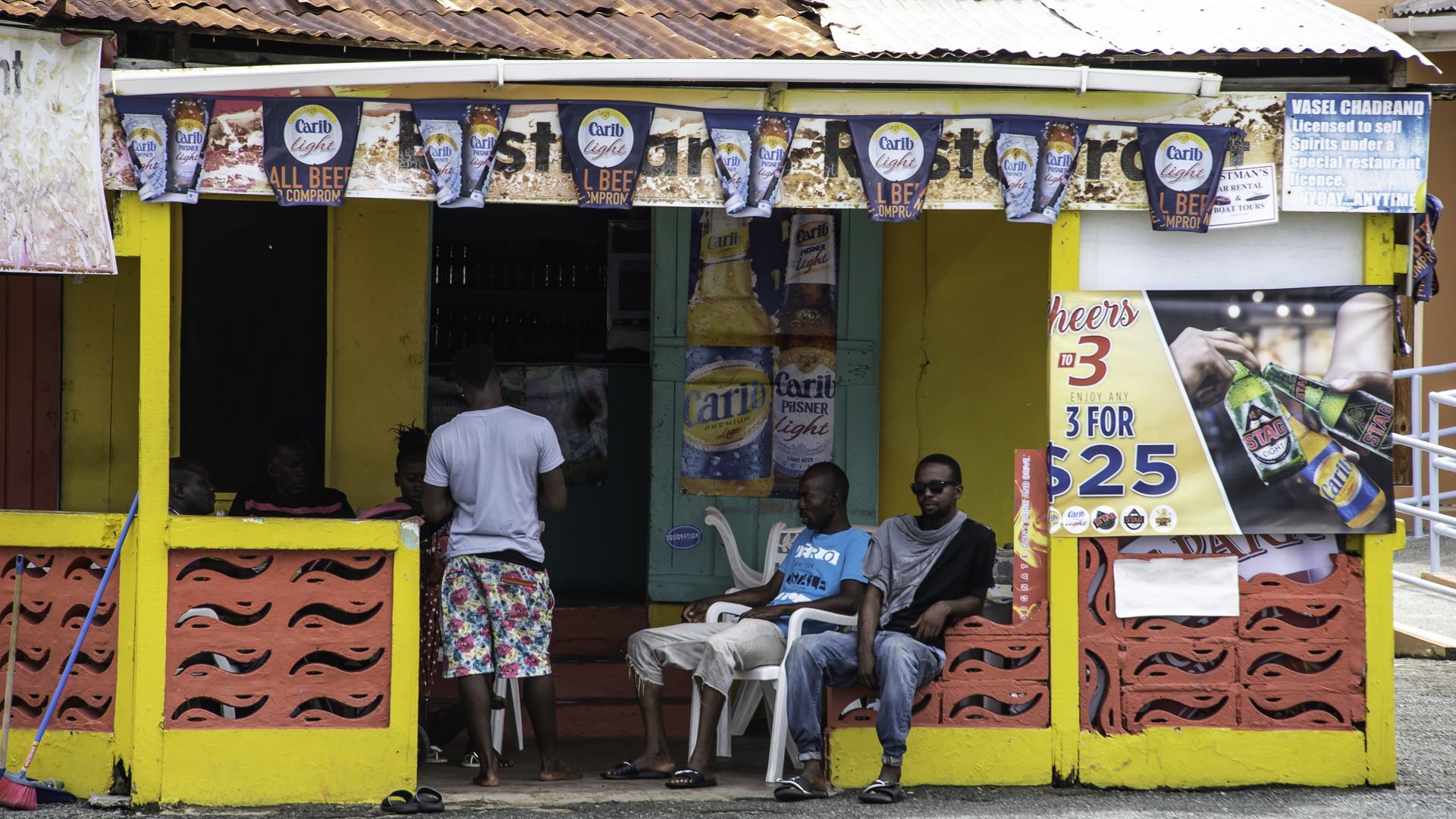 Tre siddende mænd, der taler med hinanden foran en butik i Tobago